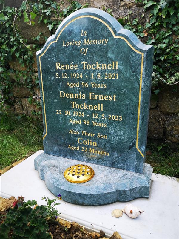 A polished green marble headstone by skilled Memorial Masons, with gold lettering, commemorates Renée, Dennis Ernest, and Colin Tocknell. The headstone is surrounded by grass, ivy, a seashell at its base, and shows signs of Grave Maintenance.